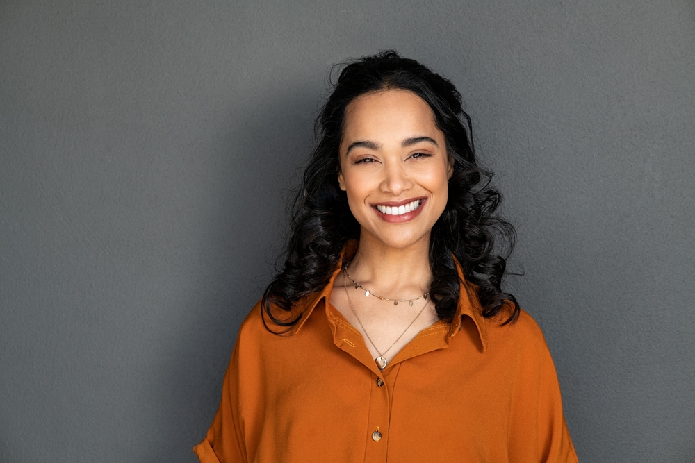 Smiling woman with a bright white smile against a grey wall