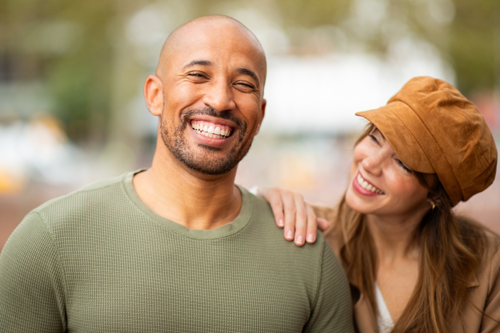 Smiling man with a woman resting her hands on his shoulders