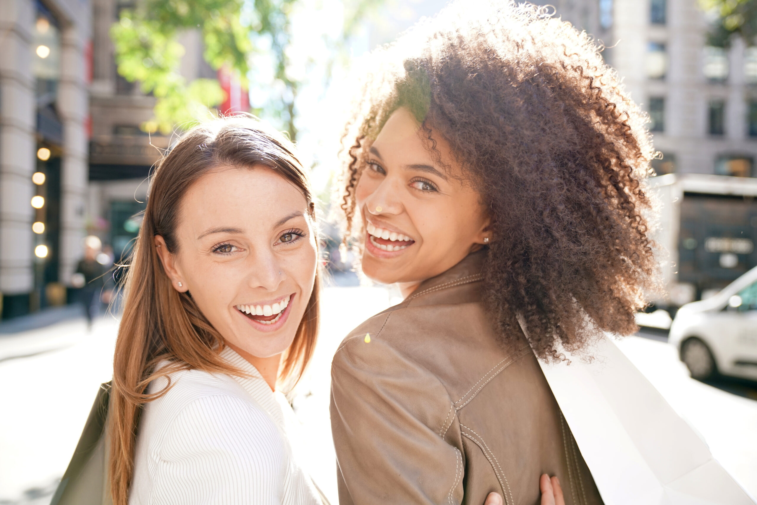 Two smiling friends looking back over their shoulders on a sunny street